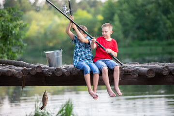 Happy friends boys caught a fish with a fishing rod. Children on a fishing trip.