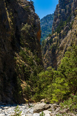 Fototapeta na wymiar Hikers in a deep gorge surrounded by spectacular cliffs during a hot summer