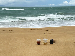 Obraz premium Three plastic cups stand in the sand, which are still partly filled with ice cofee cocktails drinks.