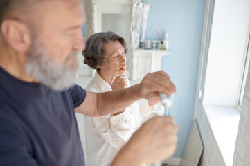 Senior married couple brushing teeth together standing at home bathroom