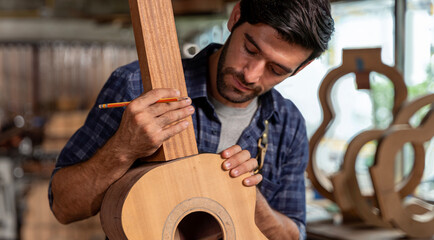 Guitar makers man making acoustic guitars in laboratory. Asian guitar maker builds high quality...