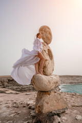 Woman sea stone. A woman stands on a stone sculpture made of large stones. She is dressed in a...