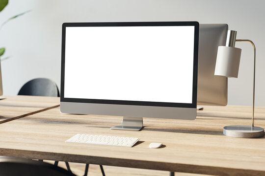 Close up of empty white computer screen on wooden office desktop with lamp and supplies on concrete wall background. Designer workplace concept. Mock up, 3D Rendering.