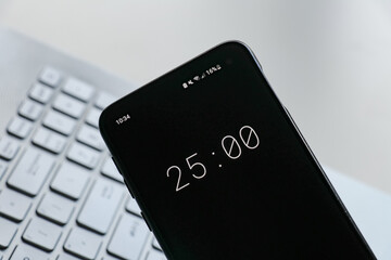 A phone with a black and white 25-minute timer to study with the pomodoro method on a blurry background. Perfect for students planning their time studying, doing homework, being productive. - obrazy, fototapety, plakaty