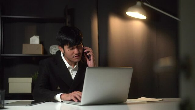 
Tired man looking at laptop working hard sleepy and office syndrome in the dark room office. Stressed asian business man working late at night hands on head feeling headache. Overtime concept.