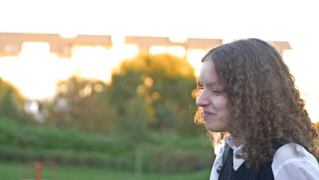 Curly-haired teenage girl inflates a big gum bubble until it bursts.