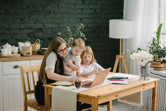 Mother working with kids at home. Woman working, learns on laptop computer. Children playing, make noise, distract, disturb mom. Angry and tired woman. Writing, typing. Communication. Maternity leave.