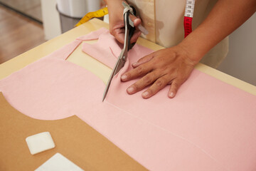 Asian female fashion designer cutting material at a studio workbench