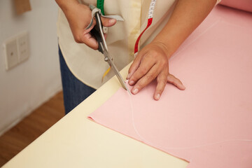 Asian female fashion designer cutting material at a studio workbench