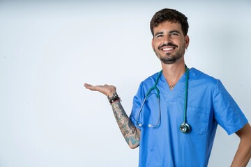 young caucasian doctor man wearing blue medical uniform smiling cheerful presenting and pointing...