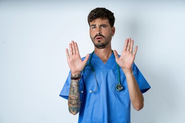 young caucasian doctor man wearing blue medical uniform Moving away hands palms showing refusal and...