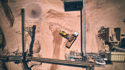 Front loader loading dumper truck with crushed stone. Stone crushing plant top down aerial view....