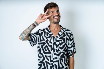 young caucasian man wearing printed shirt Doing peace symbol with fingers over face, smiling cheerful showing victory