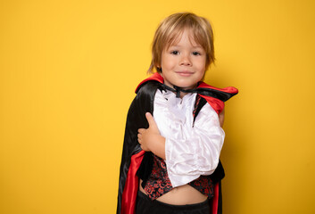 little boy dressed as a vampire on halloween isolated over yellow background. Halloween celebration...