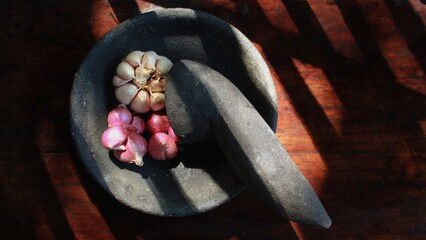 Onions and garlic on a mortar with a wooden base in the morning, with the shadow of a bamboo fence.
