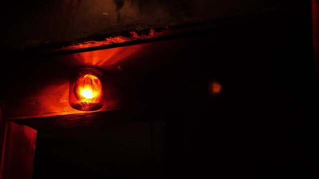Close-up of a rotating red emergency siren lamp on the wall of a dark room. A bomb shelter, an emergency signal on the wall during an air raid.
