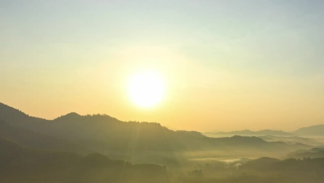 aerial hyper lapse view golden sunrise in Phang Nga valley on the mountain range..the sun shone through the fog in the valley..The yellow light from the sky illuminated the misty valley.