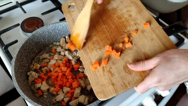 Woman adding carrots to roasted chopped chicken breast with vegetables in the pan