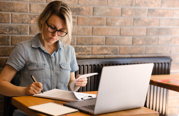 A young woman with a laptop on the table, signing business documents. A woman with glasses works in an office with documents and in a laptop. Sign a contract, a contract.