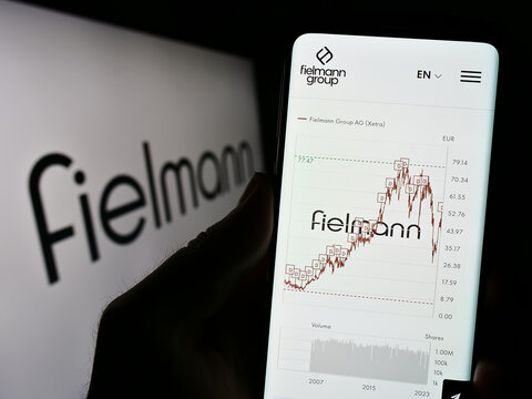 Stuttgart, Germany - 08-21-2023: Person holding cellphone with webpage of German eyewear company Fielmann AG on screen in front of logo. Focus on center of phone display.