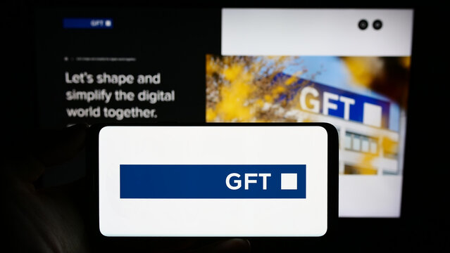 Stuttgart, Germany - 08-21-2023: Person holding smartphone with logo of German IT company GFT Technologies SE on screen in front of website. Focus on phone display.