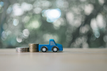 Blue miniature pickup model and coins pile on green nature background. Finance and car loan concepts. Concept savings to buy a new car or journey insurance.