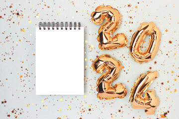Empty notepad mockup, glowing stars confetti and 2024 golden inflatable balloons on a blue pastel...