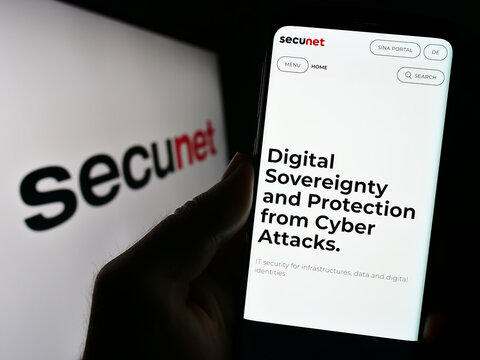 Stuttgart, Germany - 08-22-2023: Person holding cellphone with webpage of German company secunet Security Networks AG on screen in front of logo. Focus on center of phone display.