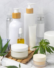 Fototapeta na wymiar Blank cosmetic jars, tubes and bottles near green cannabis leaves close up, CBD cosmetic mockup