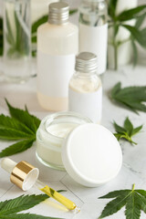 Fototapeta na wymiar Cream jar with a blank lid and pipette with CBD oil near cannabis leaves