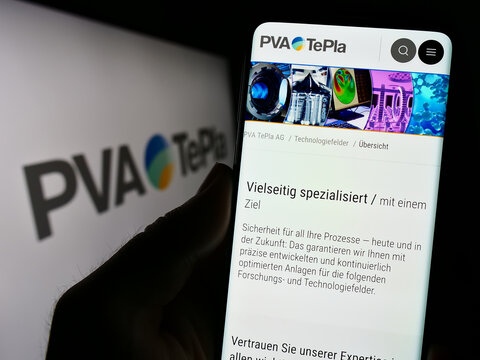 Stuttgart, Germany - 08-22-2023: Person holding smartphone with webpage of German technology company PVA TePla AG on screen in front of logo. Focus on center of phone display.