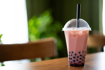 Milk bubble tea in takeaway glass on table in cafe blurred background