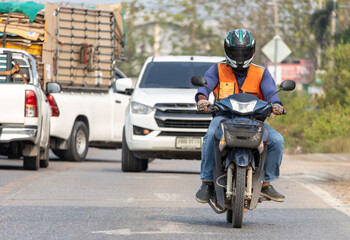 Front view of a man in an orange vest of a taxi driver riding a motorcycle, Bangkok, Thailand