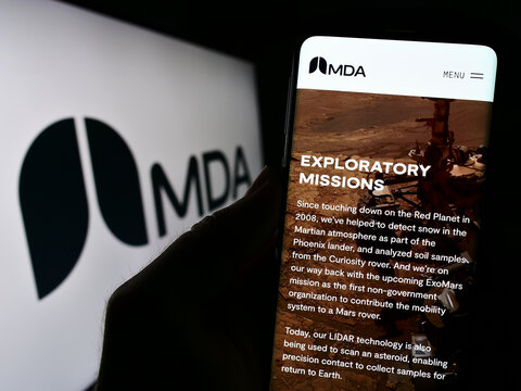 Stuttgart, Germany - 08-25-2023: Person holding cellphone with website of Canadian space technology company MDA Ltd. on screen in front of logo. Focus on center of phone display.