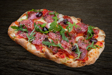Pizza Diavolo with chorizo, rucola, jalapeno, chili, kalamata, pesto. Roman pizza rectangular on wood background