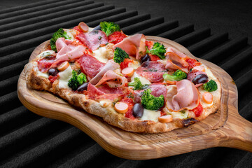 Pizza with salami, ham, vienna sausages, kalamata, olives, broccoli, pelati, pesto. Roman pizza rectangular on dark background