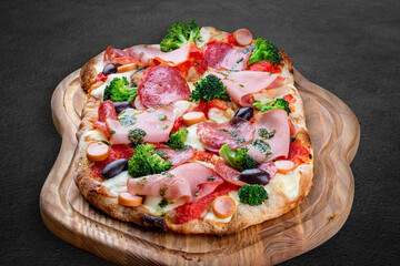 Pizza with salami, ham, vienna sausages, kalamata, olives, broccoli, pelati, pesto. Roman pizza rectangular on dark background