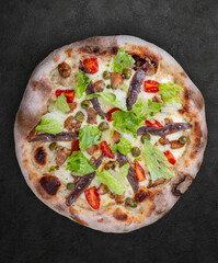 Caesar pizza with chicken, anchovies, romaine, cherry, kalamata, capers, pesto. Neapolitan round pizza on dark background
