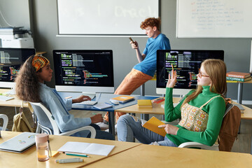 Group of students sitting at desk with computers during IT lesson in the classroom