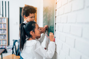 Group of little child standing at chalkboard and writing math formula on blackboard in classroom at school, education concept.	