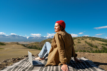 woman freelancer traveler working online using laptop and enjoying the beautiful nature landscape with mountain view.