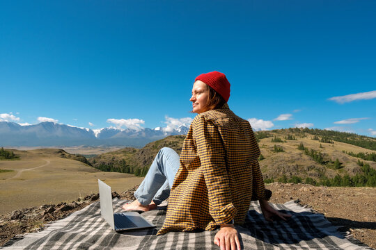 woman freelancer traveler working online using laptop and enjoying the beautiful nature landscape with mountain view.