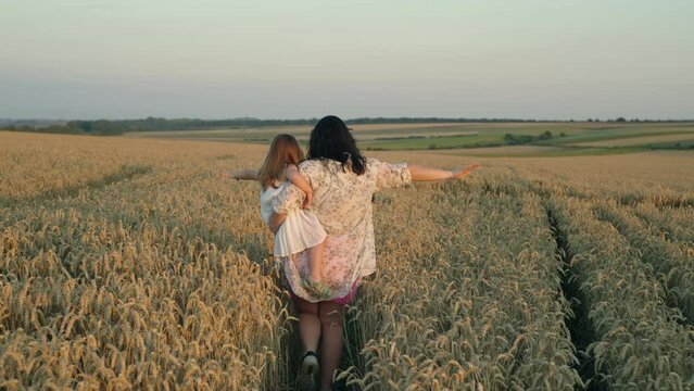 Mom holds her daughter in her arms and runs across the wheat field. The happy family melted their hands and flies. Freedom happiness concept. Growing grain in agricultural fields. High quality 4k 