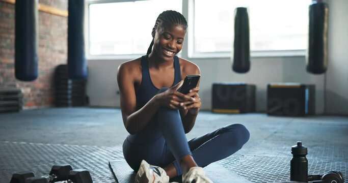 Smile, fitness and black woman with a cellphone, typing or social media with workout, relax or connection. African person on the floor, health or girl with a smartphone, mobile app or chat on a break