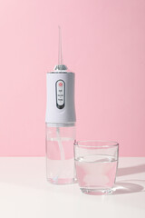 Irrigator and glass of water on table on pink background