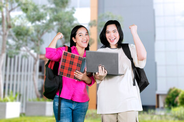 Excited young asian girls holding laptop computer and notebook celebrating success