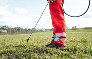 Farmer spraying pesticide on lawn field wearing protective clothing. Treatment of grass from weeds...
