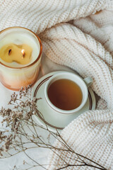 Fototapeta na wymiar Home decor. Knitted blanket, candle, hot cup of tea, dried flowers. Cozy autumn.