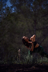 Hispanic woman doing Revolved Chair asana in nature