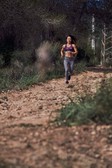 Fototapeta na wymiar Serious athletic ethnic lady jogging on path in woods